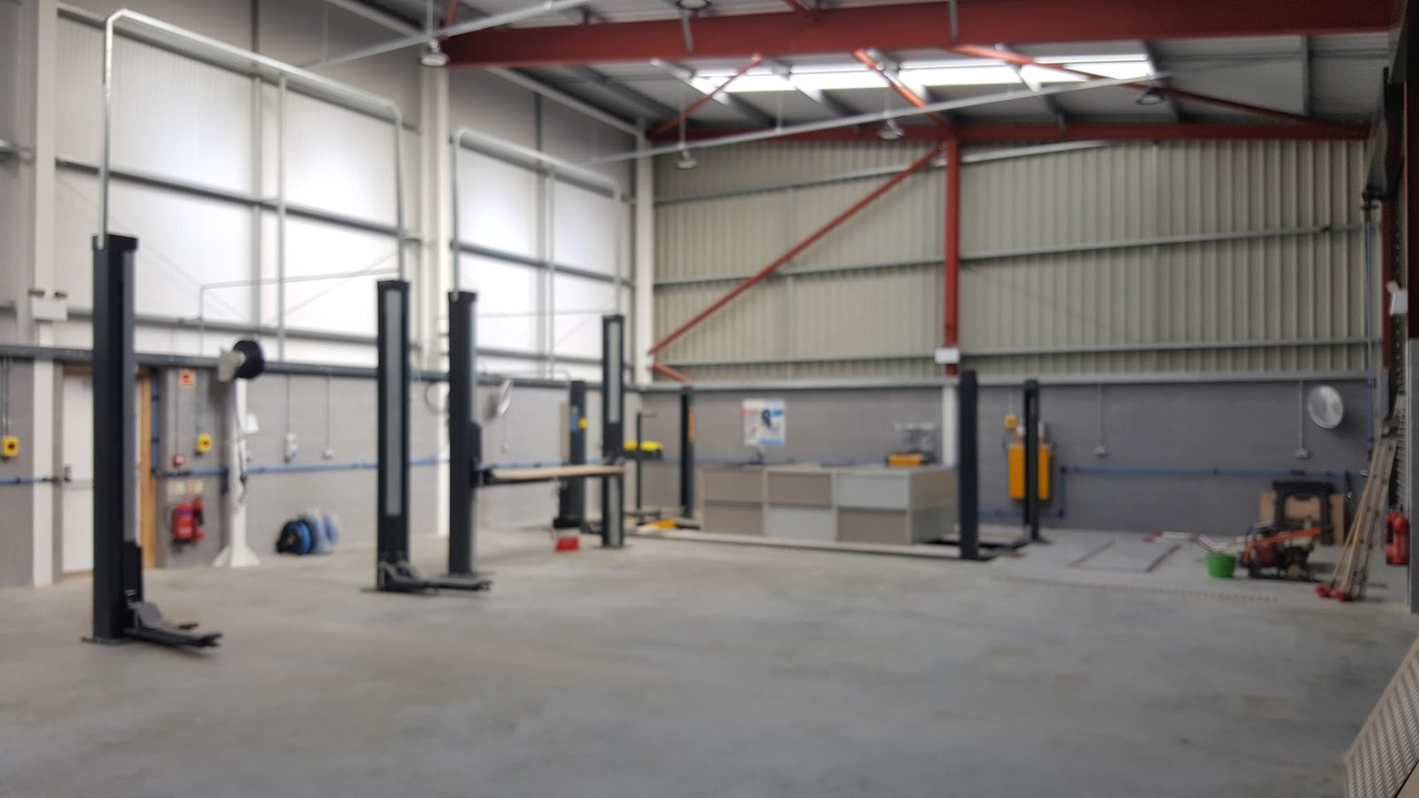Inside the empty workshop: a row of two-post vehicle lifts under red steel roof beams