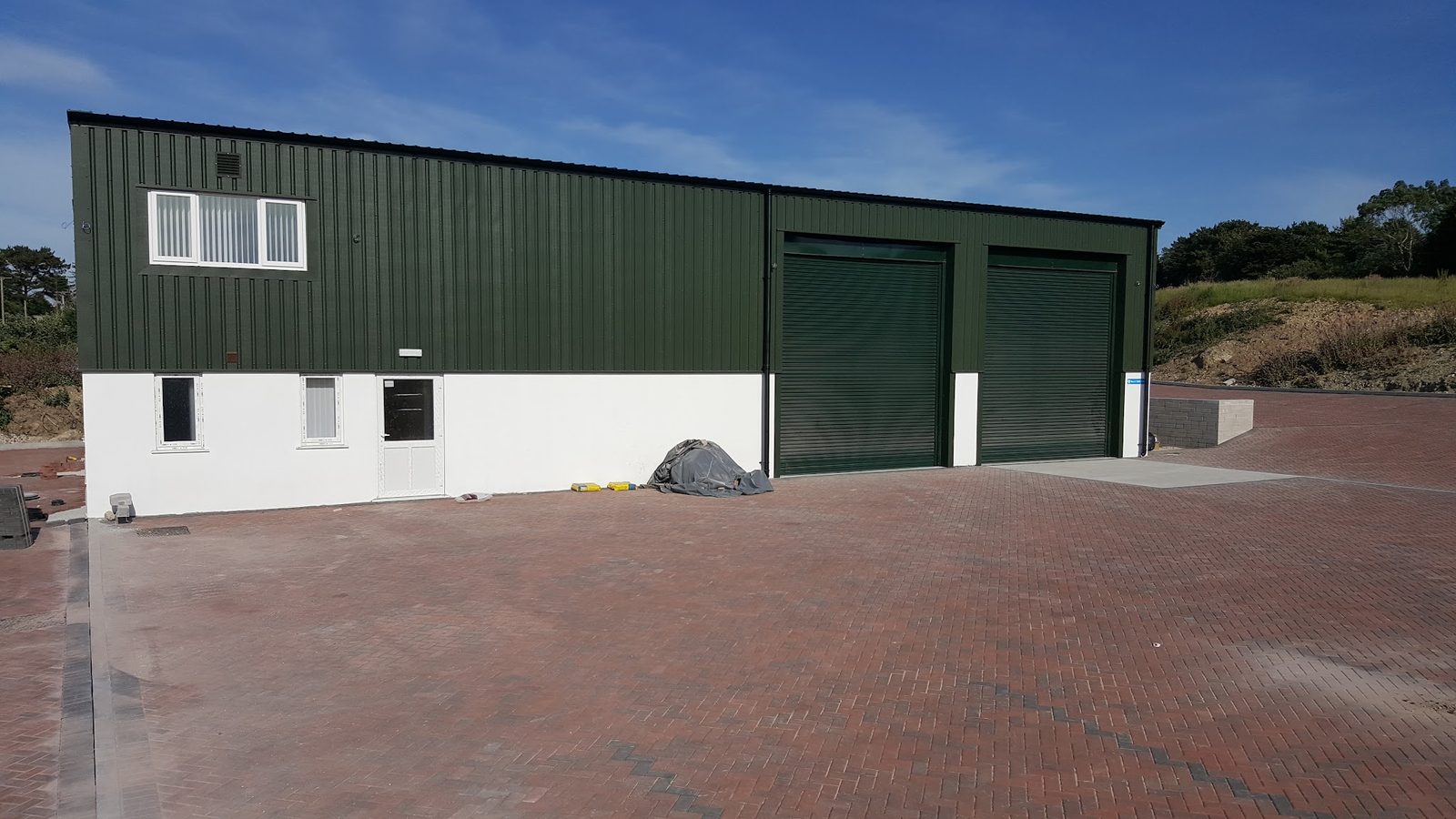 The finished green-clad workshop with two green roller doors and a large brick-paved yard